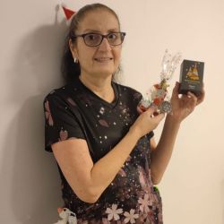 Eine Frau mit Brille im festlichen Outfit hält fröhlich Geschenke, während sie ein rotes Partyhütchen amüsiert trägt.