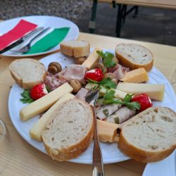 Ein Teller mit Brot, Käse, Schinken und Tomaten ist dekorativ mit bunten Servietten und Besteck auf einem Tisch angerichtet.