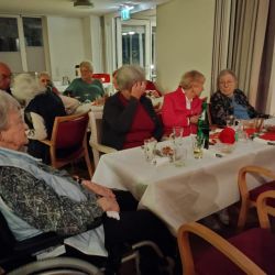 Ältere Menschen genießen fröhlich Gespräche an einem festlich gedeckten Tisch in einem gemütlichen Raum.