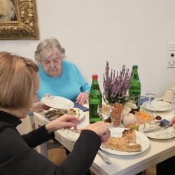 Drei Personen sitzen am Tisch, genießen Kuchen und Wasser, während eine Frau in Blau konzentriert auf ihr Essen schaut.