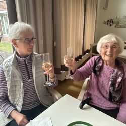 Zwei ältere Damen stoßen mit Sektgläsern an und genießen einen fröhlichen Moment zusammen.