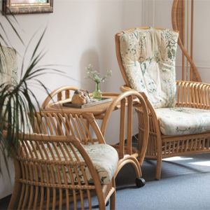 Zwei gemütliche Rattan-Sessel stehen einladend neben einem kleinen Tisch in einem hellen Raum mit Pflanzen.