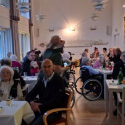 In einem gemütlichen Raum sitzen Menschen unterschiedlichen Alters an Tischen und unterhalten sich lebhaft miteinander.