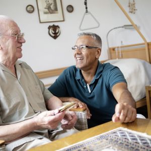 Ein älterer Mann und ein jüngerer Mann lächeln herzlich bei einem freundlichen Gespräch in einem gemütlichen Raum.