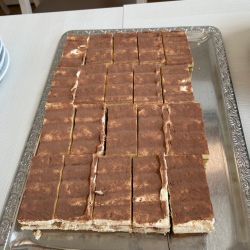 Ein Tablett voller rechteckiger Tiramisu-Stücke steht auf einem Tisch, bereit für den Genuss.
