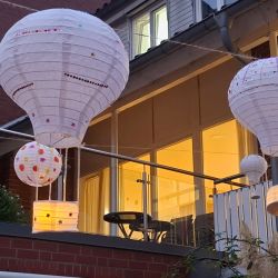 Bunte Papierlaternen in Form von Heißluftballons schmücken eine Terrasse bei Dämmerung.