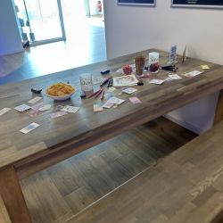 Ein Holztisch ist voller bunter Stifte, Notizen und Snacks in einem hellen Raum mit großen Fenstern im Hintergrund.