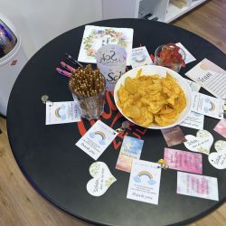 Auf einem runden Tisch liegen Chips und Brezeln neben inspirierenden Karten mit Regenbogenmotiven und Danksagungen.