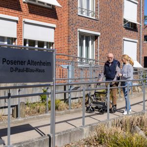 Eine Frau begleitet einen älteren Mann am Posener Altenheim auf einer Rampe im Freien. | © Name