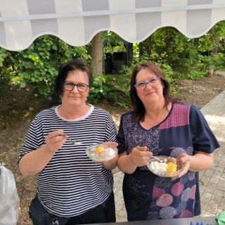 Zwei Frauen genießen Eis in Schalen unter einem schattigen Pavillon an einem sonnigen Tag im Freien.