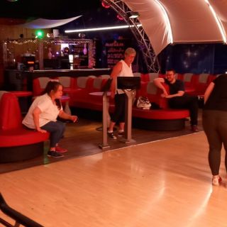 In einer Bowlingbahn entspannen Menschen auf roten Sofas neben der glänzenden Kegelbahn und plaudern fröhlich.
