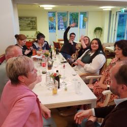 Eine Gruppe von Menschen sitzt fröhlich um einen Tisch in einem gemütlichen Raum und genießt zusammen Getränke.