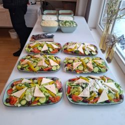 Sechs bunte Salatteller mit Feta und Oliven stehen auf einem Tisch, bereit für ein Buffet oder ein Event.