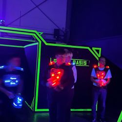 Personen spielen Lasertag in einer neonbeleuchteten Arena und tragen leuchtende Westen und Ausrüstungen.