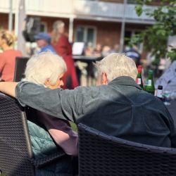 Ein älteres Paar sitzt eng umschlungen im Garten und genießt gemeinsam die Sonne im Freien.