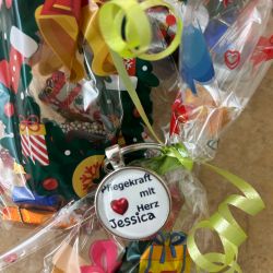 Ein festlich verpacktes Geschenk mit einer Plakette "Pflegekraft mit Herz Jessica" zeigt bunte Schleifen und Muster.