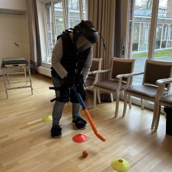 Eine Person spielt in einem Raum ein Geschicklichkeitsspiel mit einem blauen und orangefarbenen Schläger zwischen Hütchen.