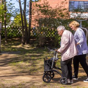 Zwei Frauen gehen im Park, eine nutzt einen Rollator zur Unterstützung beim Gehen.