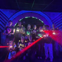 Eine Gruppe von Freunden posiert mit Laser-Pistolen in einem bunten, futuristischen Spielraum.