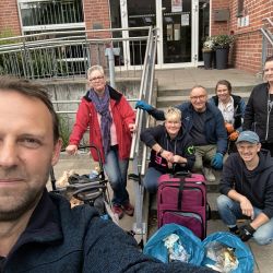 Sechs Personen lächeln vor einem Gebäude und posieren stolz mit Müllsäcken bei einer Aufräumaktion.