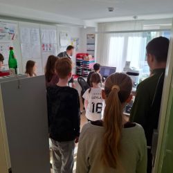 Kinder schauen gebannt auf einen Computerbildschirm in einem Raum voller Unterlagen und Materialien. | © Name