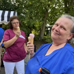 Zwei Frauen in bunten Uniformen genießen fröhlich Eis im Freien vor einem Hintergrund aus Bäumen.